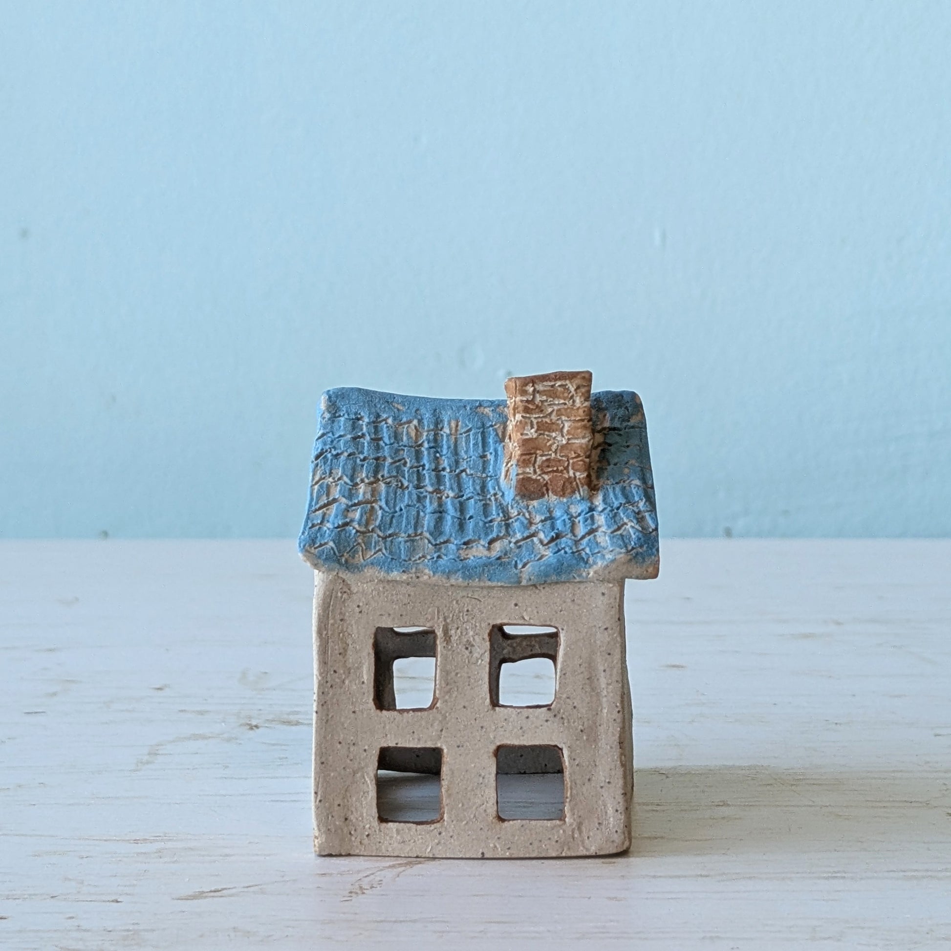 Small ceramic house with a blue roof on a light wooden surface against a light blue background