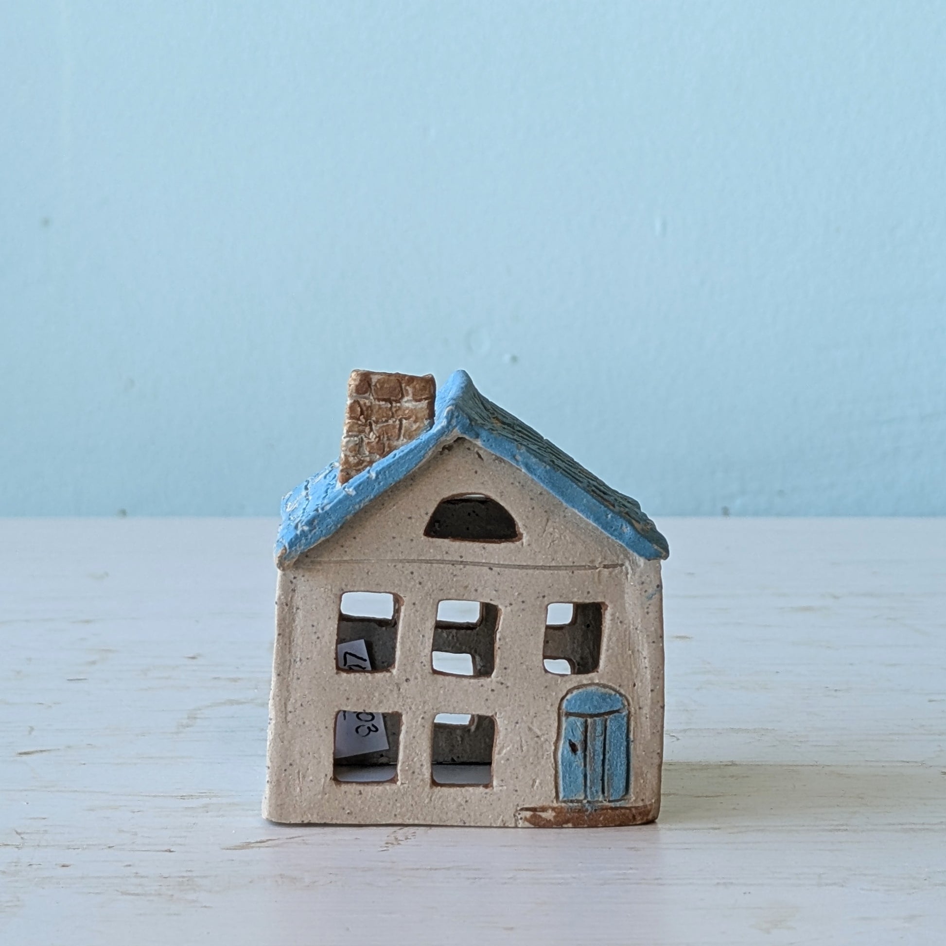 Small ceramic house with blue roof on a light wooden surface and blue background