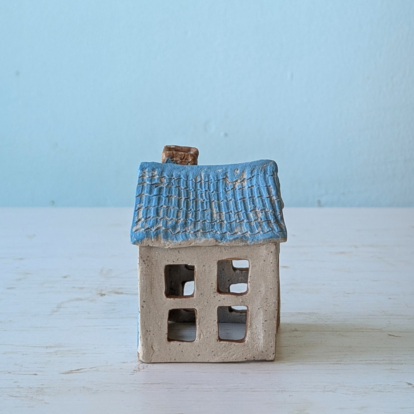 Small ceramic house with blue roof on a light wooden surface and blue background