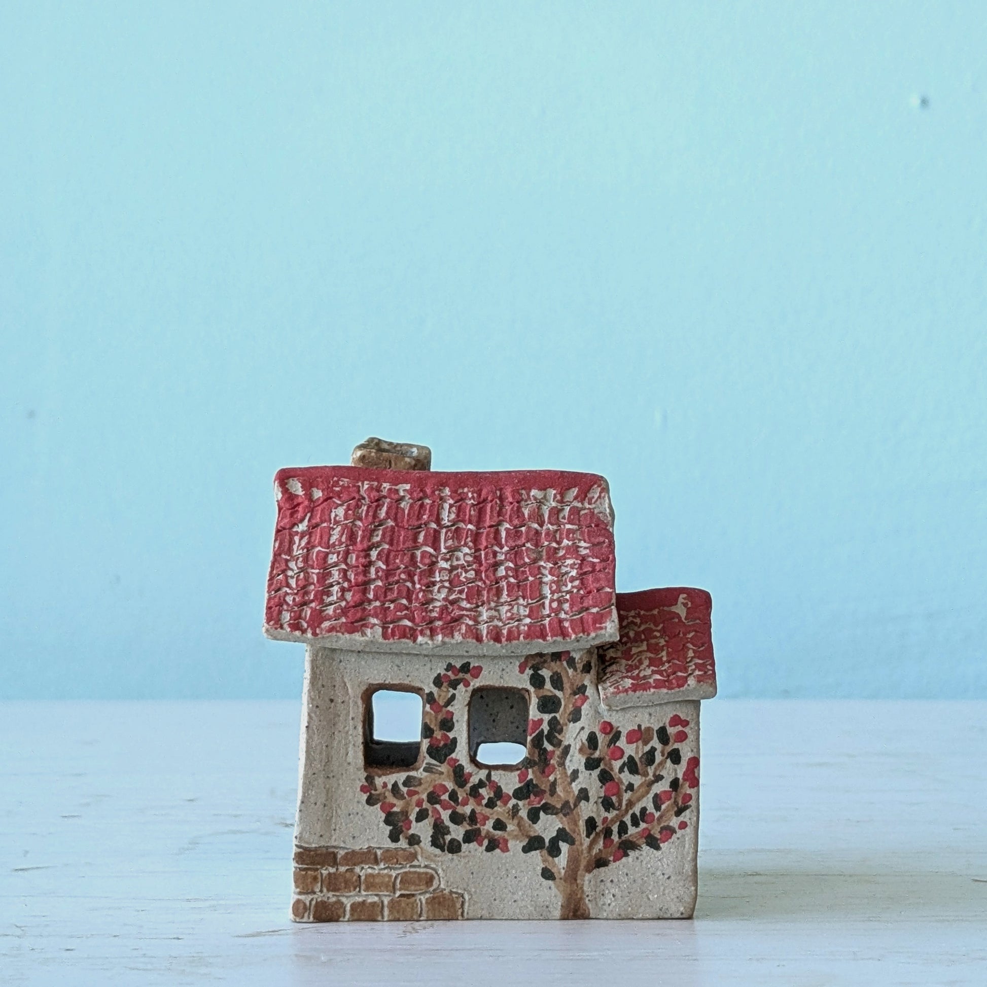 Small ceramic house with a red roof on a light blue background