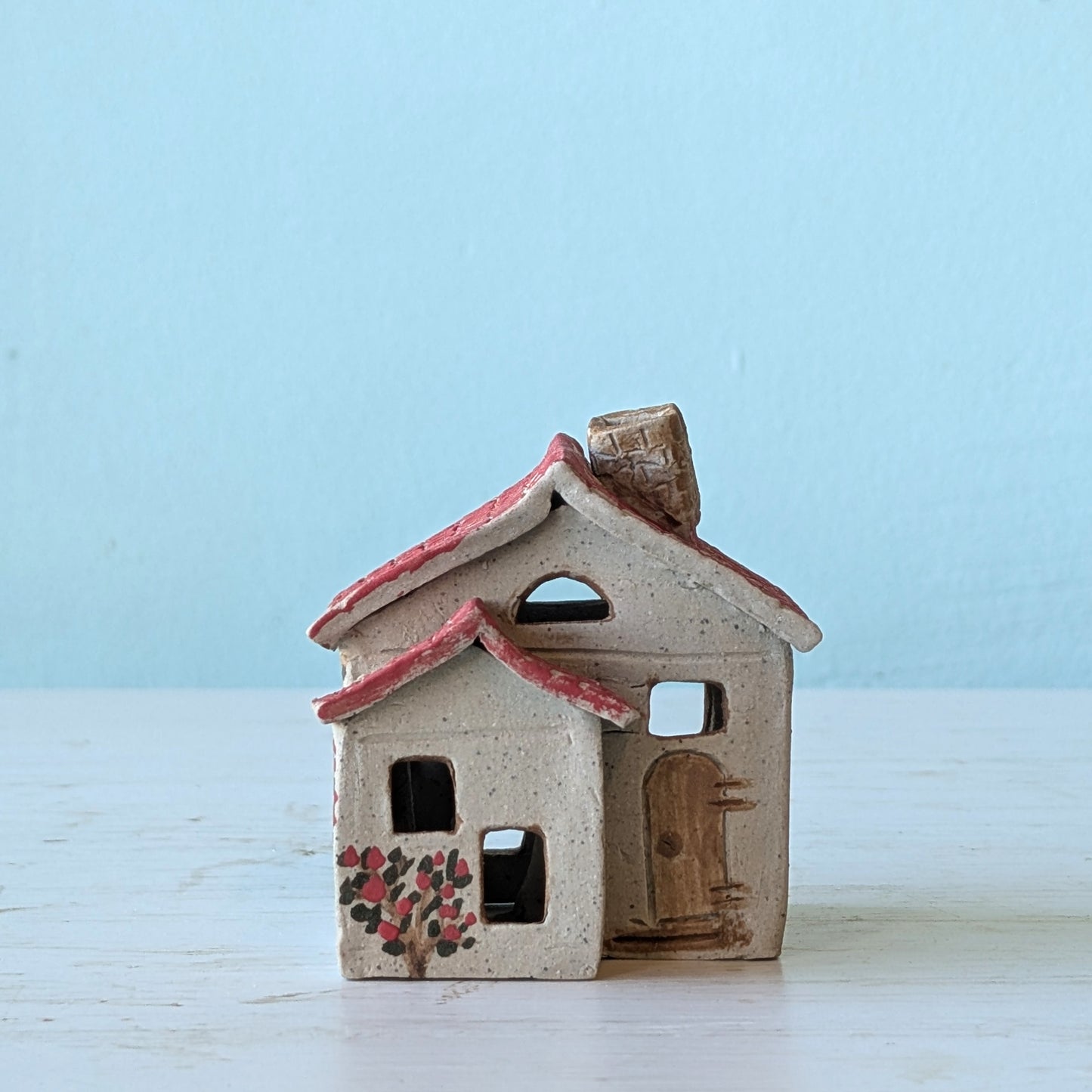Small ceramic house with a red roof on a light blue background