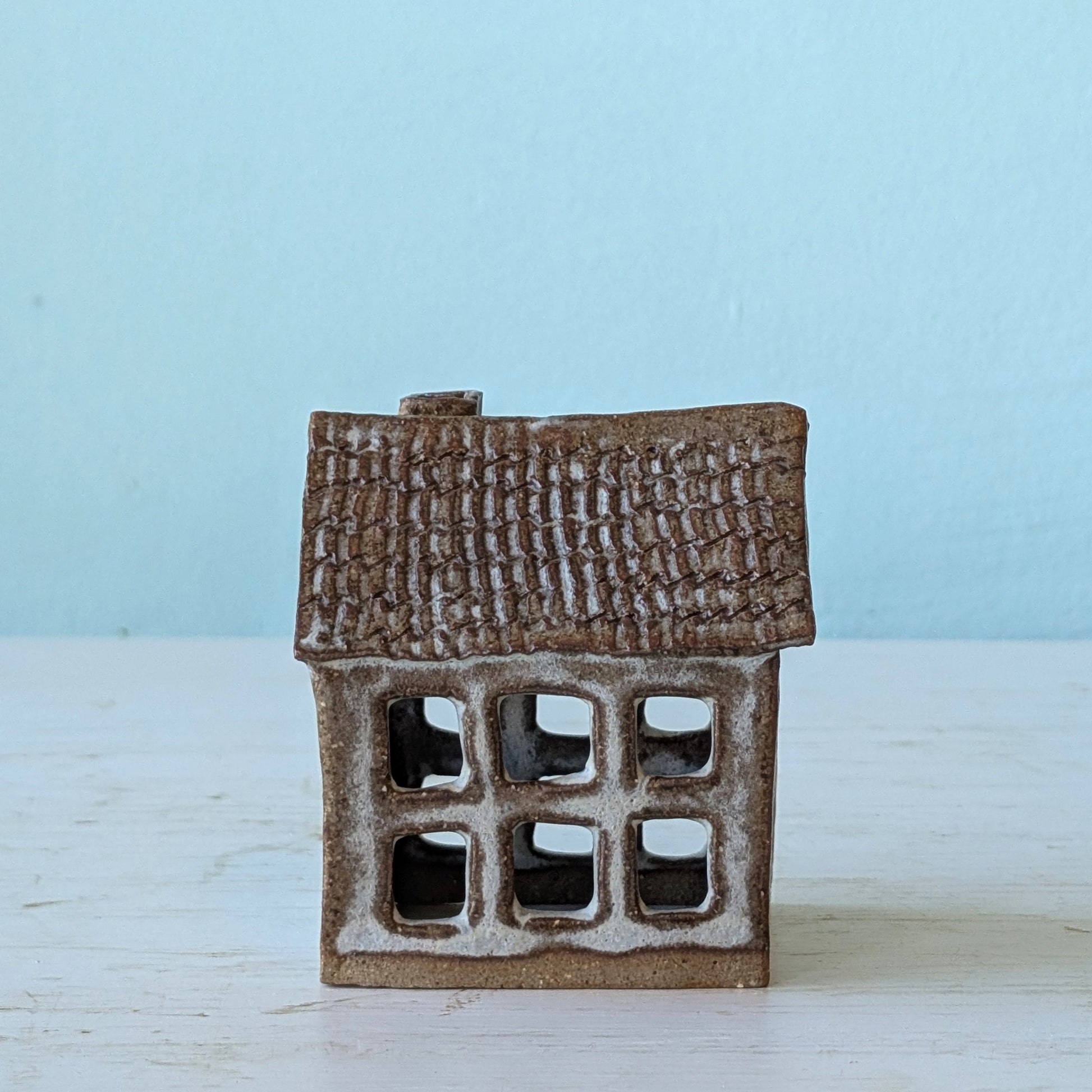 Small ceramic house figurine with textured brown roof on a light blue background