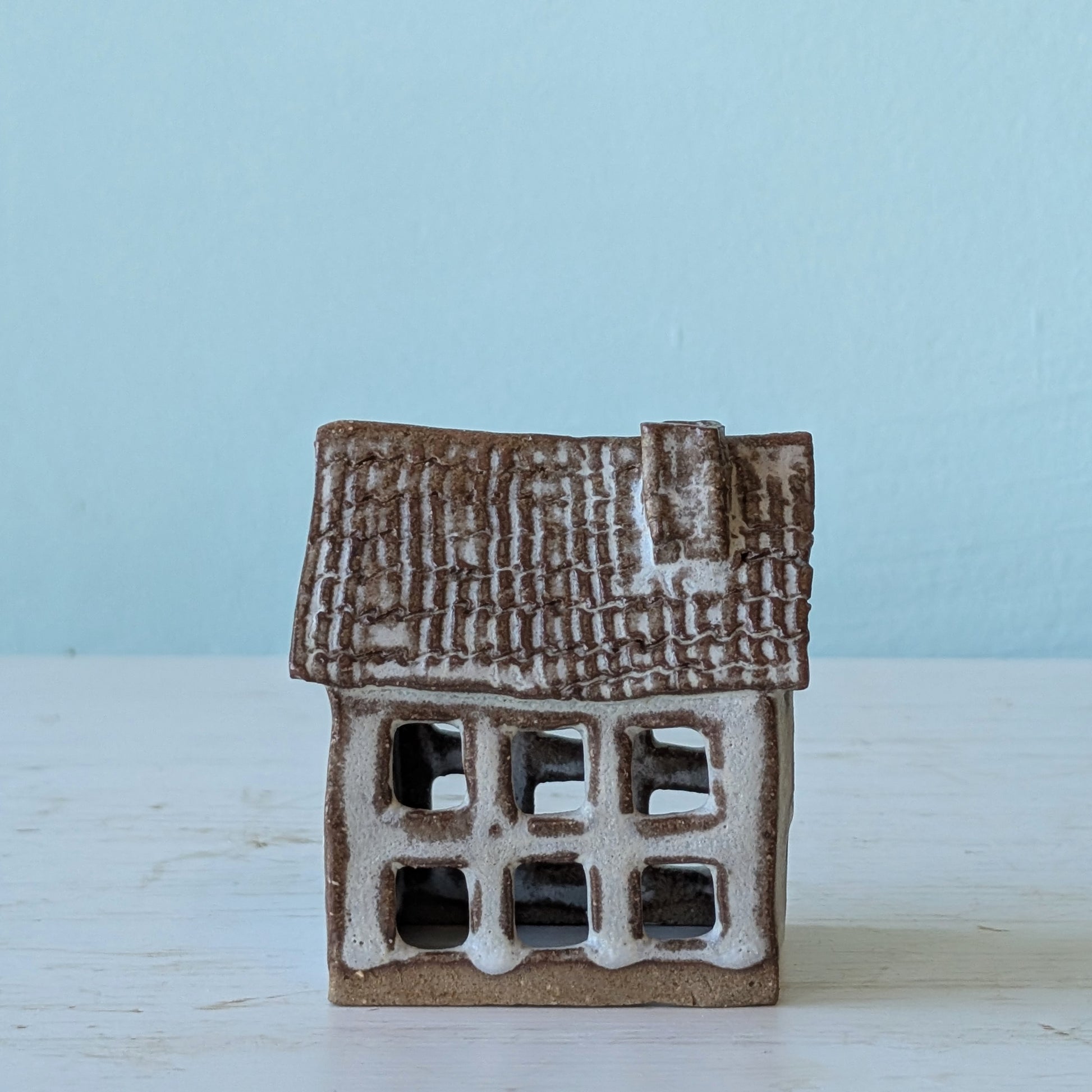 Small ceramic house with a brown roof on a light blue background
