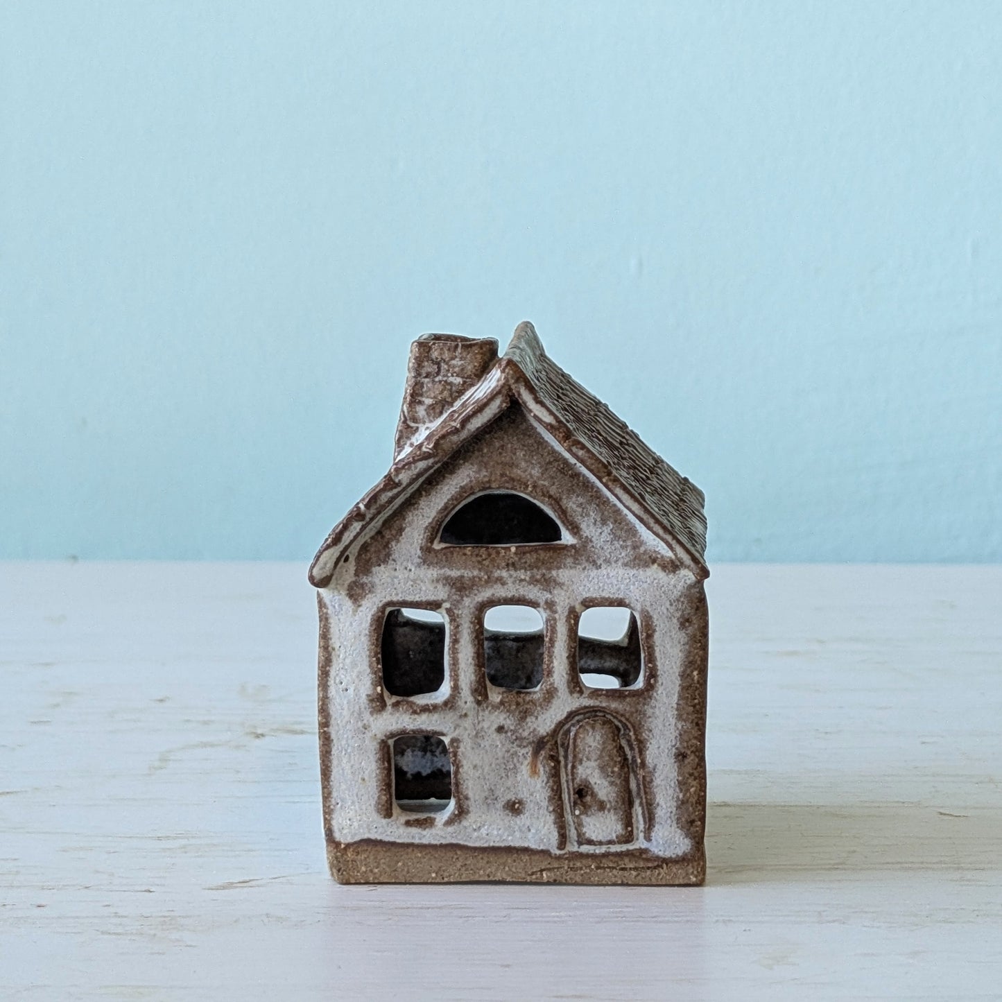 Small ceramic house-shaped object on a light wooden surface with a light blue background