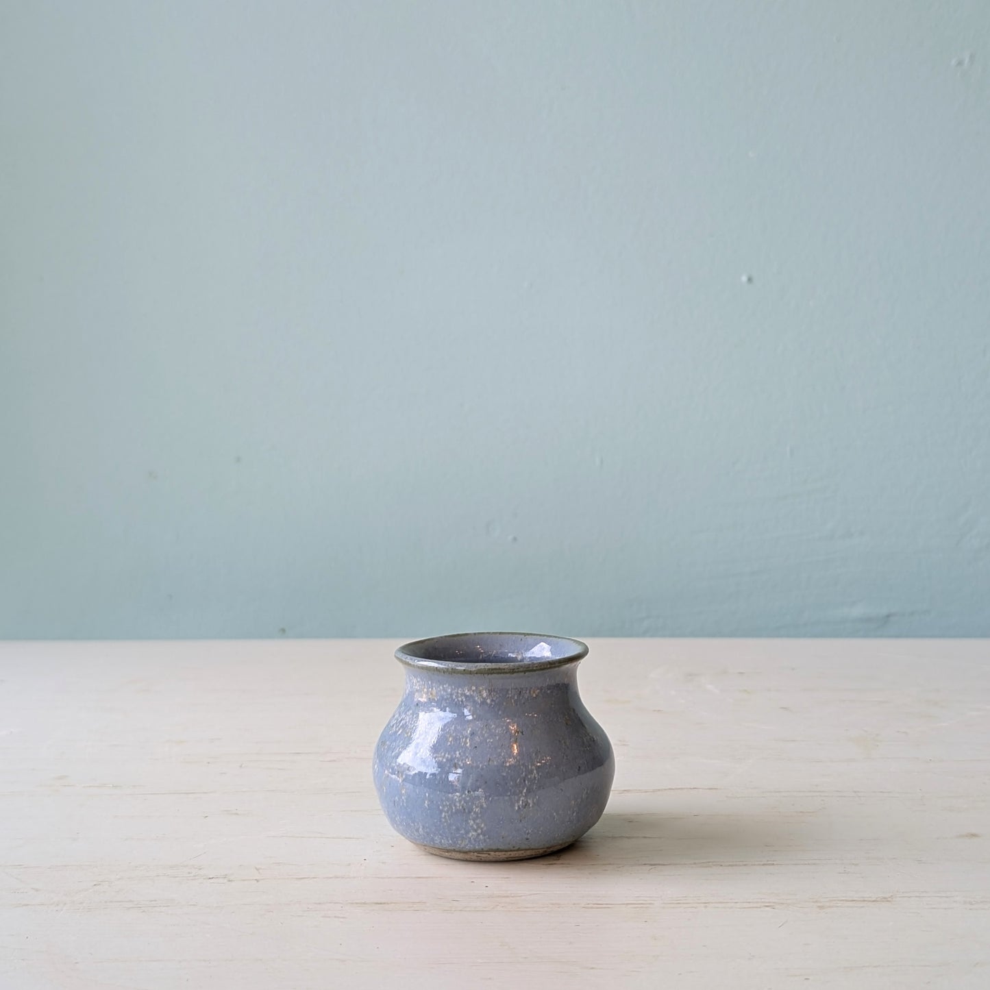 Small blue vase on a white table against a blue wall