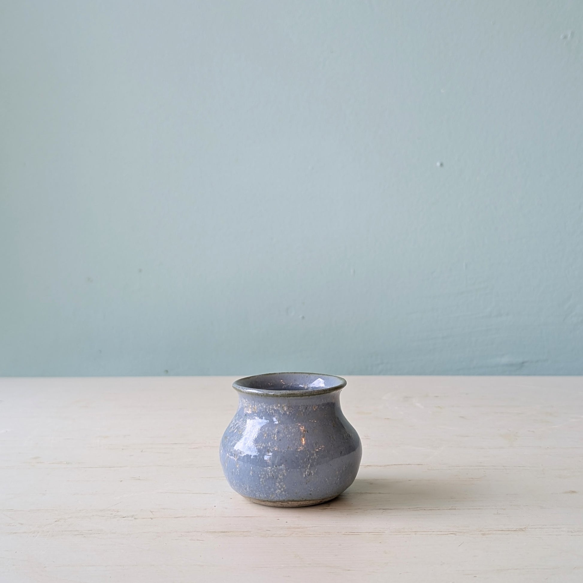 Small blue vase on a white table against a blue wall