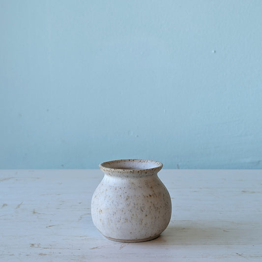 Small ceramic vase on a light wooden surface with a light blue background
