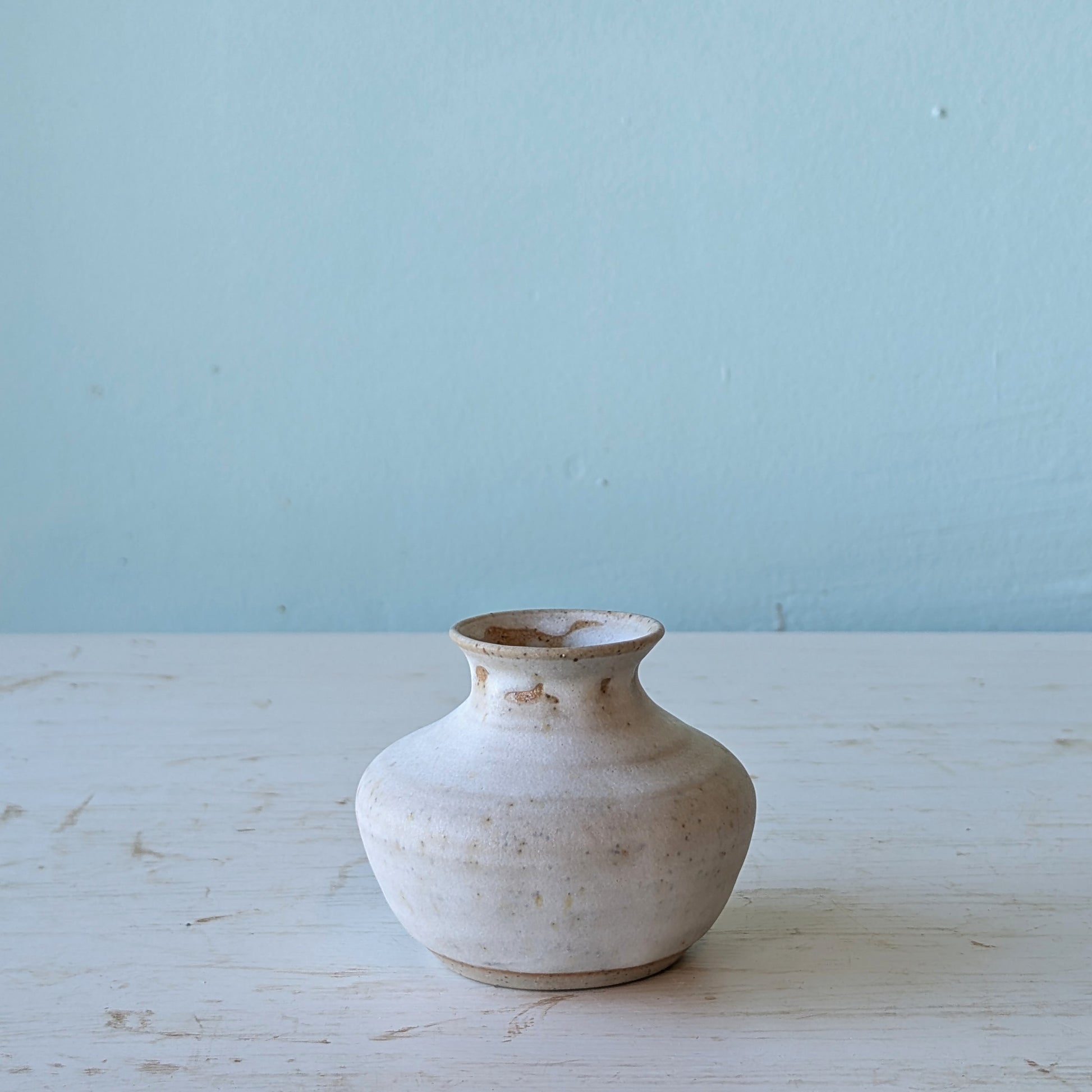 White ceramic vase on a light wooden surface with a light blue background