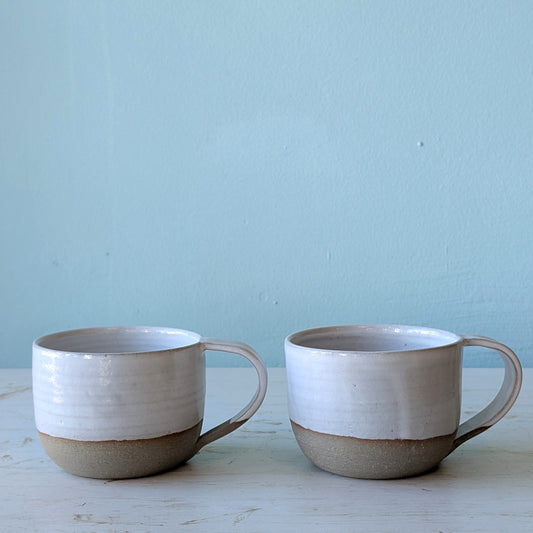 Two ceramic mugs with a two-tone design on a light blue background