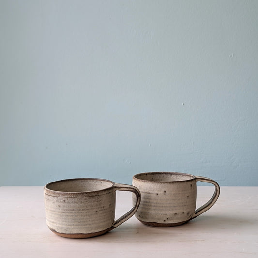 Two beige and brown ceramic coffee mugs on a white table against a blue wall