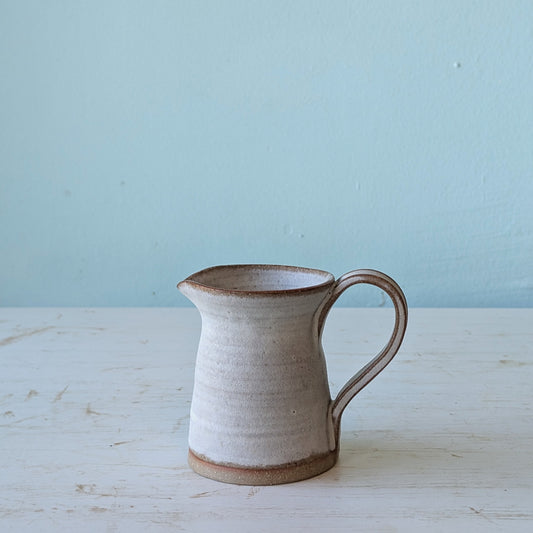 Ceramic pitcher with a handle on a light wooden surface and blue background
