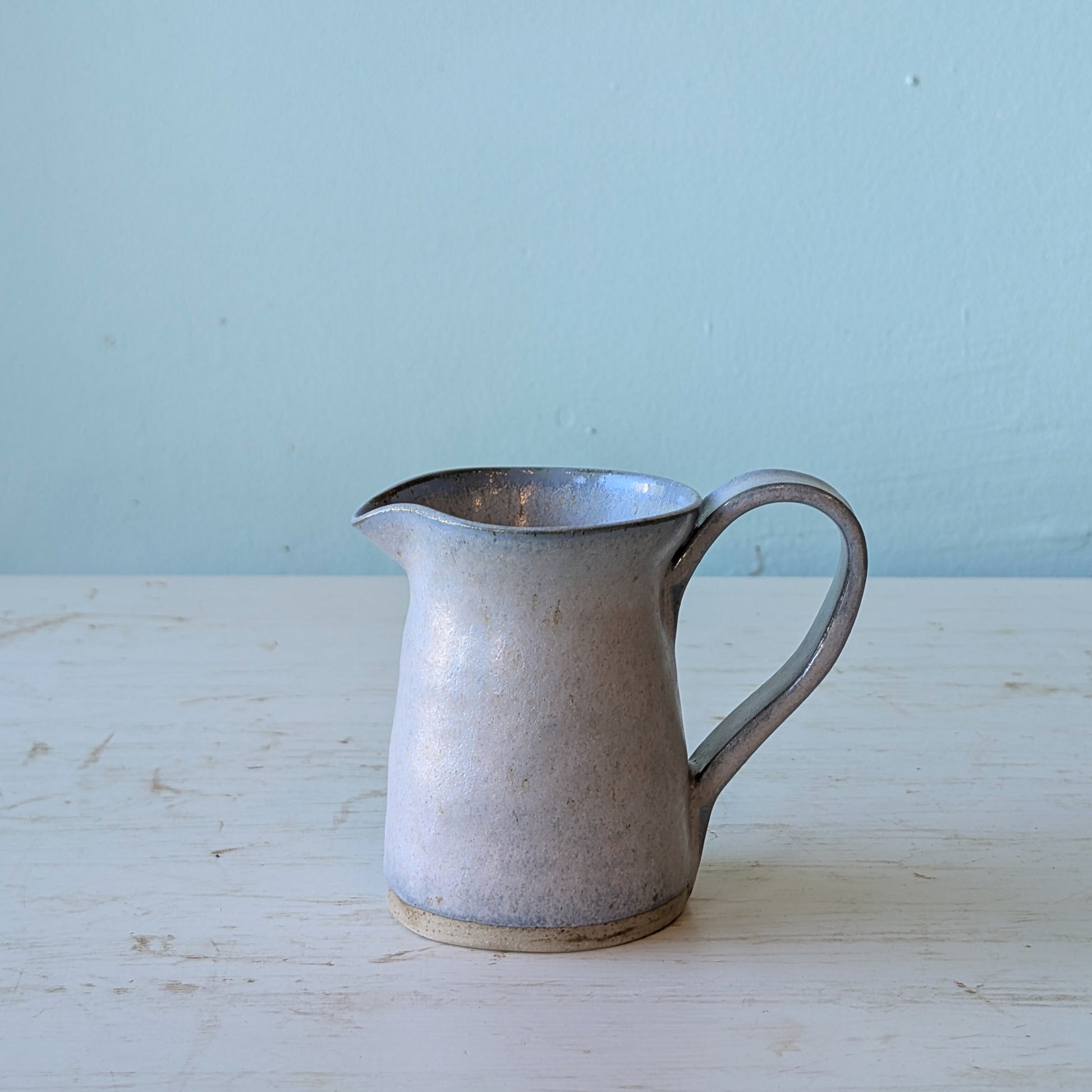Blue ceramic pitcher on a white table against a blue background