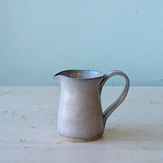Blue ceramic pitcher on a white table against a blue background