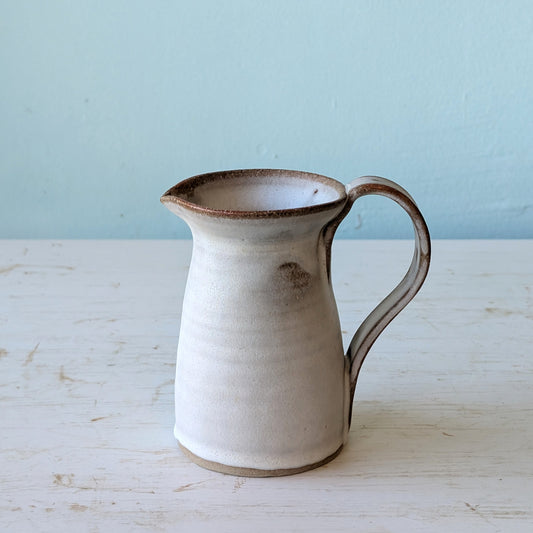 White ceramic pitcher with brown accents on a light blue background