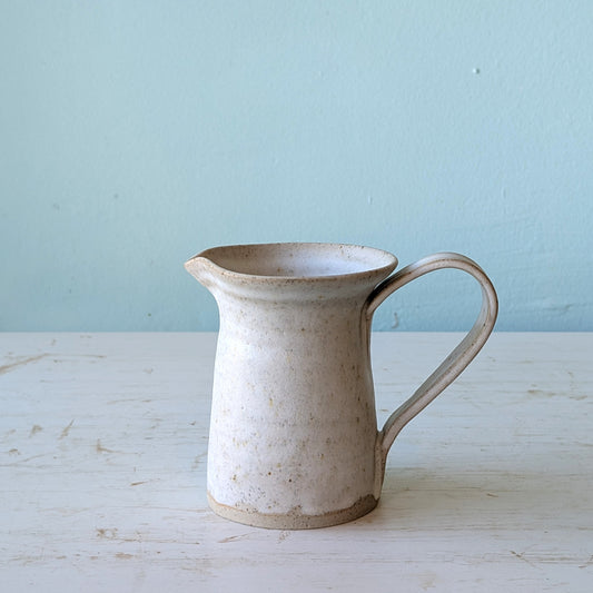 White ceramic jug on white wooden table against a blue wall
