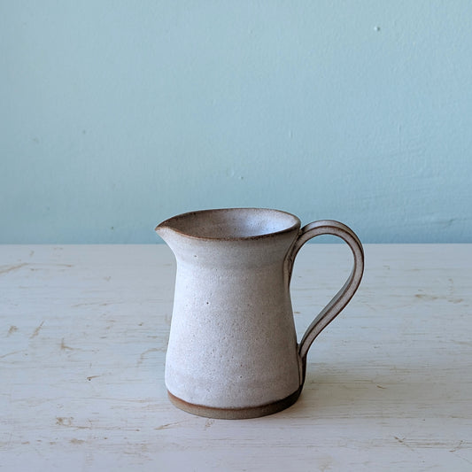 Ceramic pitcher on a wooden surface with a light blue background
