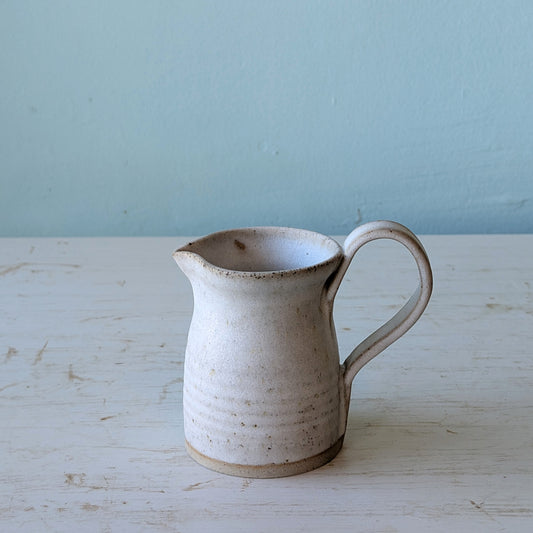White ceramic pitcher on a white wooden table against a blue wall
