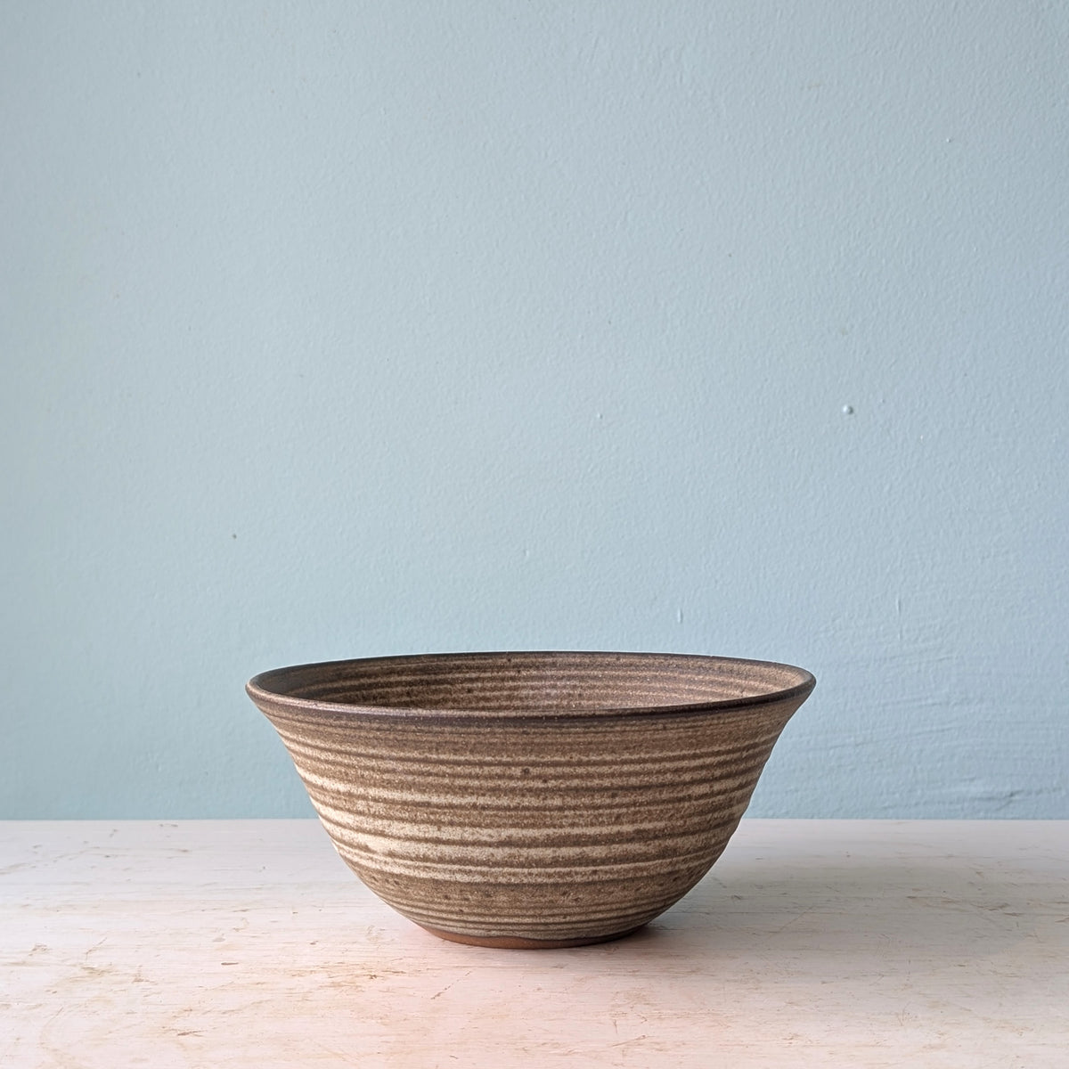 Dark brown ceramic bowl on a white wooden table against a blue wall.