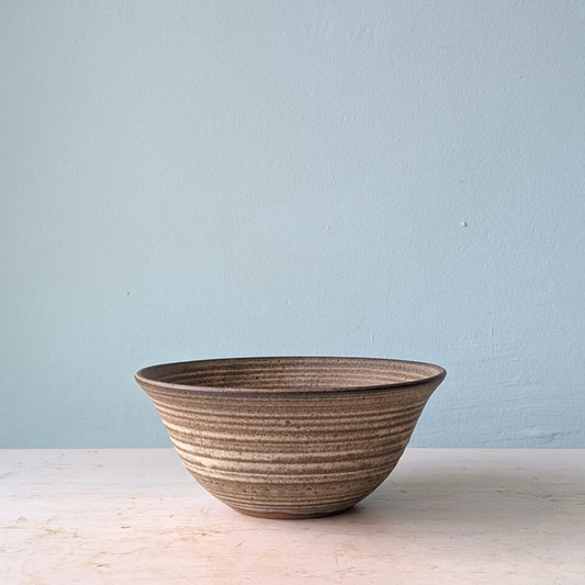 Dark brown ceramic bowl on a white wooden table against a blue wall.