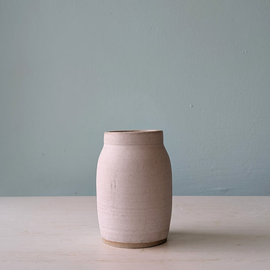 Beige ceramic vase on a light wooden surface with a light blue wall background