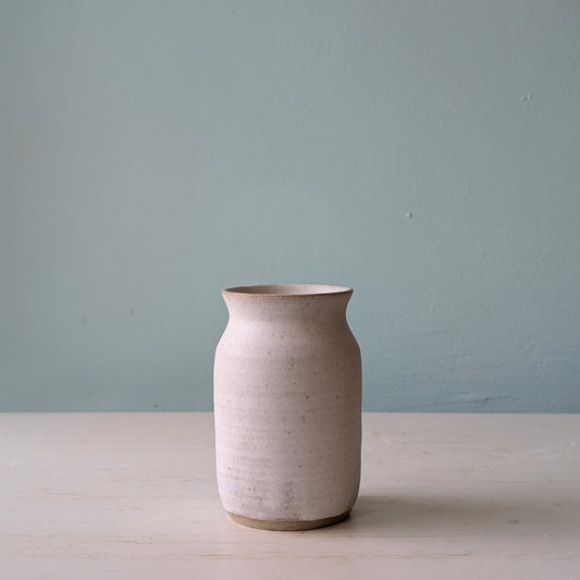 Beige ceramic vase on a light wooden surface with a light blue wall background