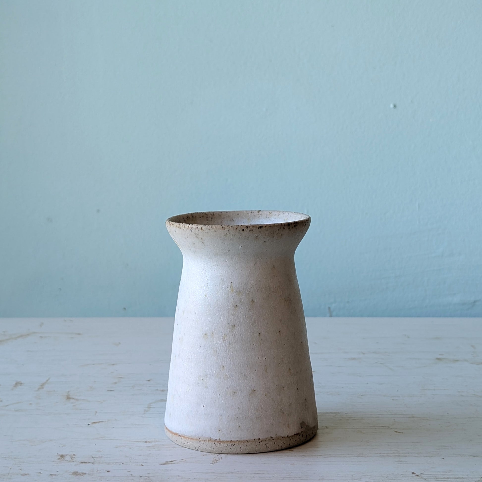 White ceramic vase on white wooden table against blue wall