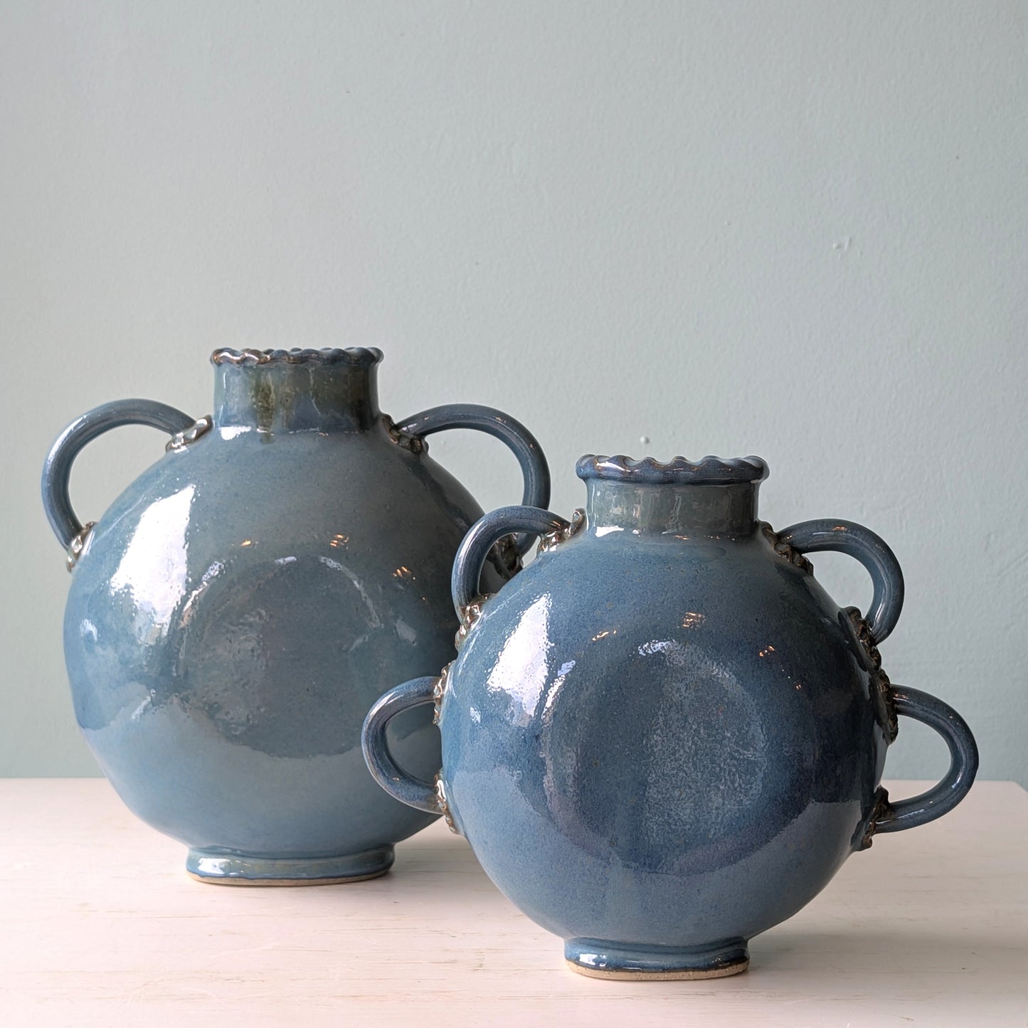 Two blue ceramic vases with handles on a light surface and blue background
