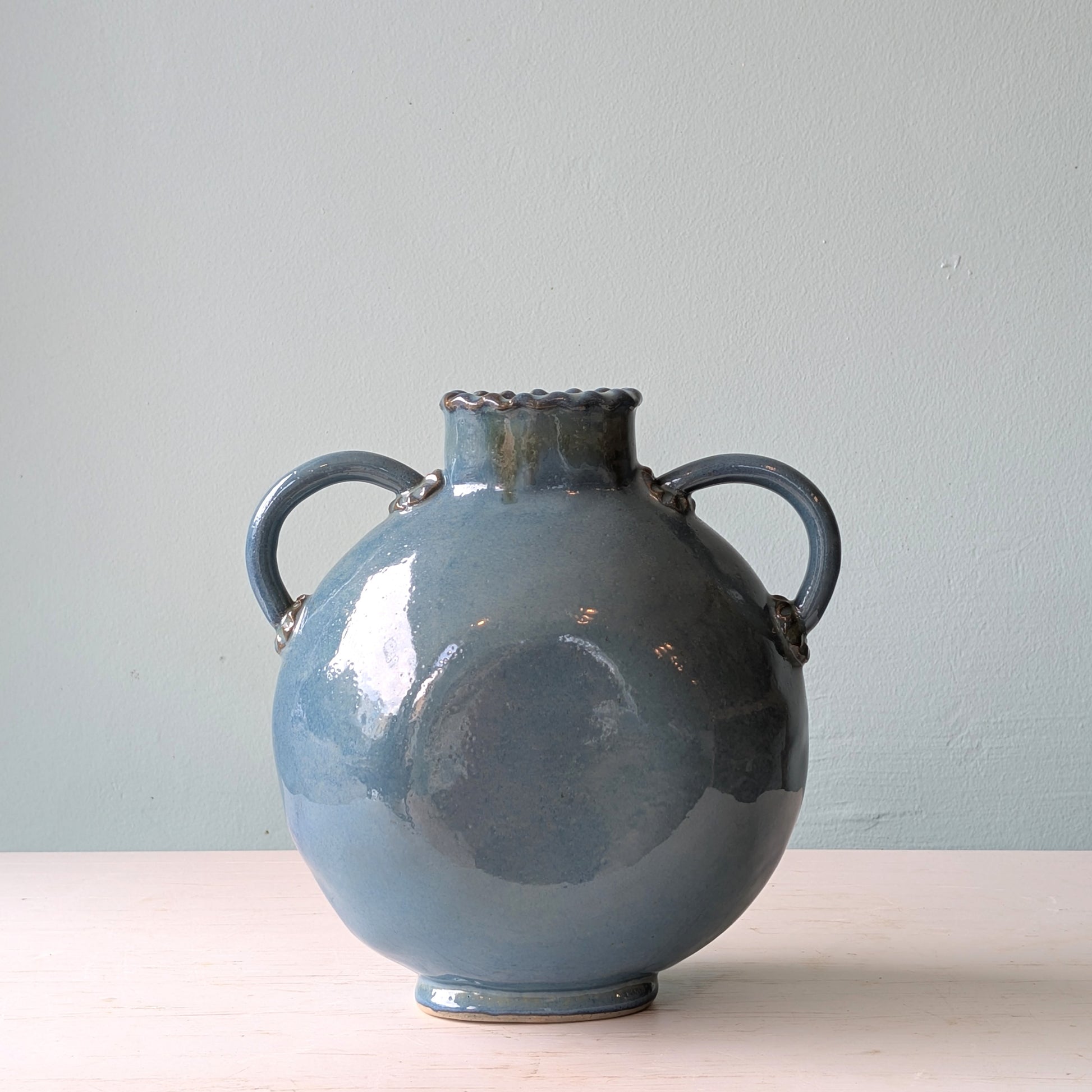 Blue ceramic vase with two handles on a light blue background