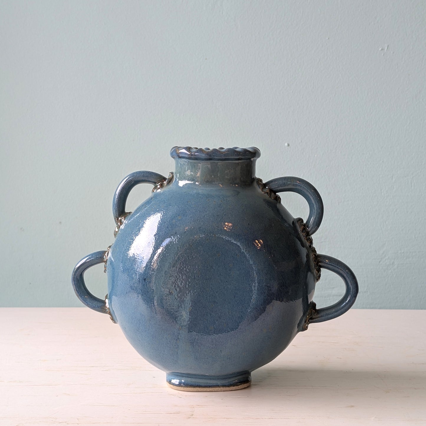 Blue ceramic vase with handles on a light surface and light blue background