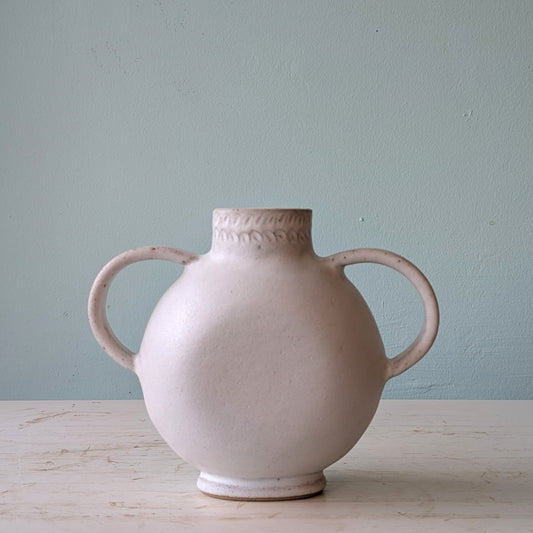 White ceramic amphora vase with two looped handles on a white table against a blue wall