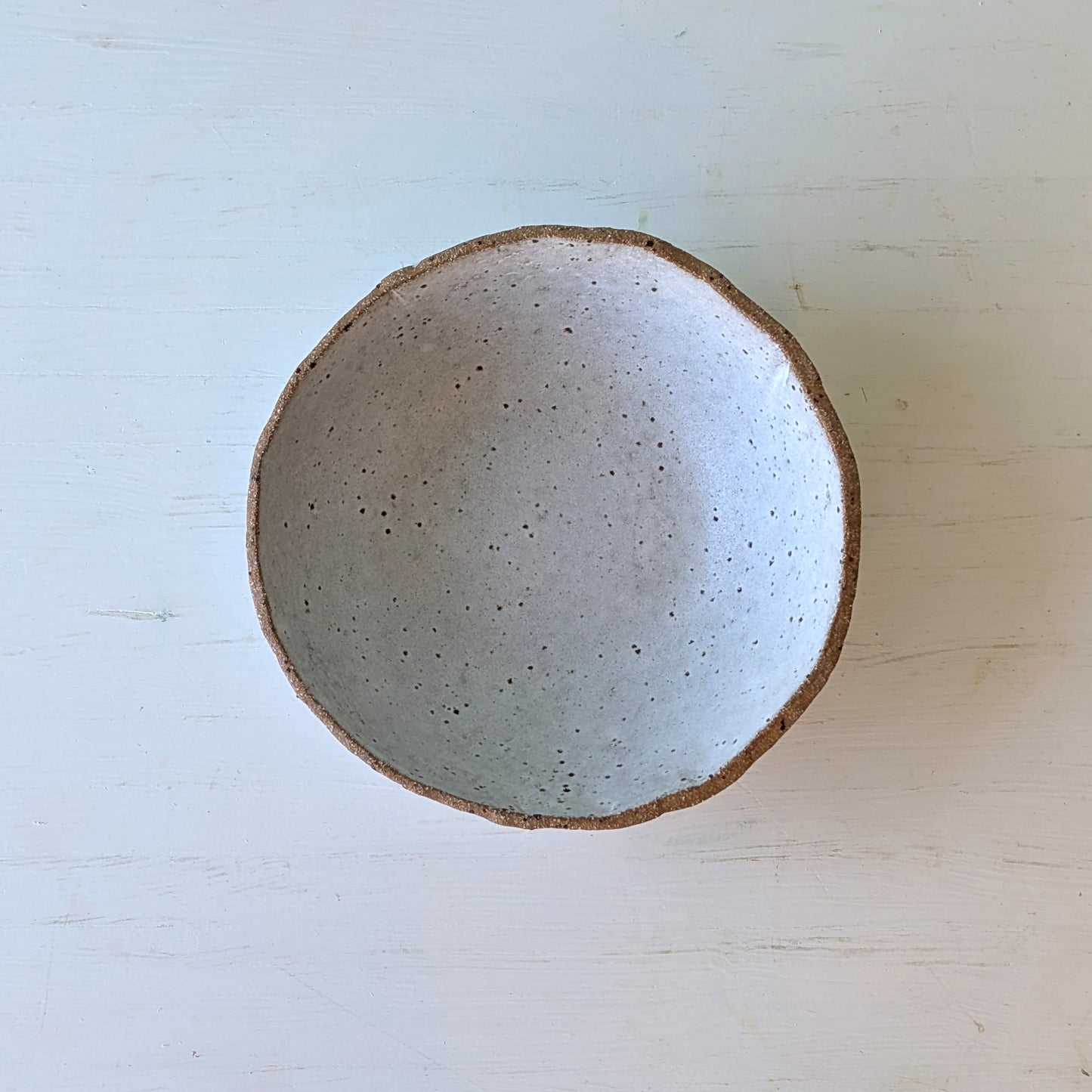 Ceramic bowl with speckled texture on a light wooden surface
