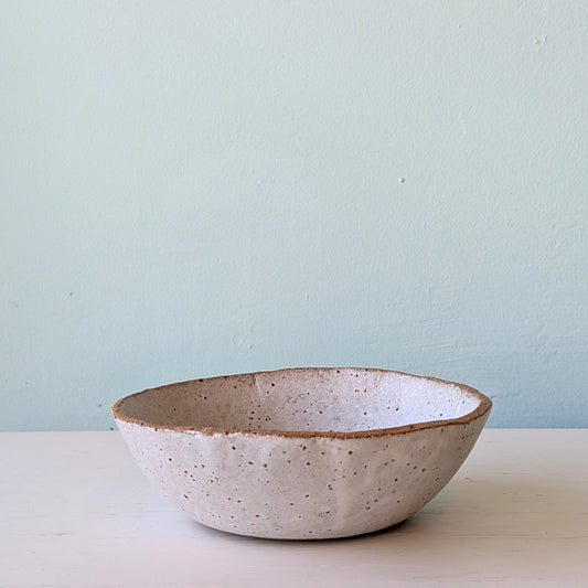 White speckled ceramic bowl on a white surface with blue background.