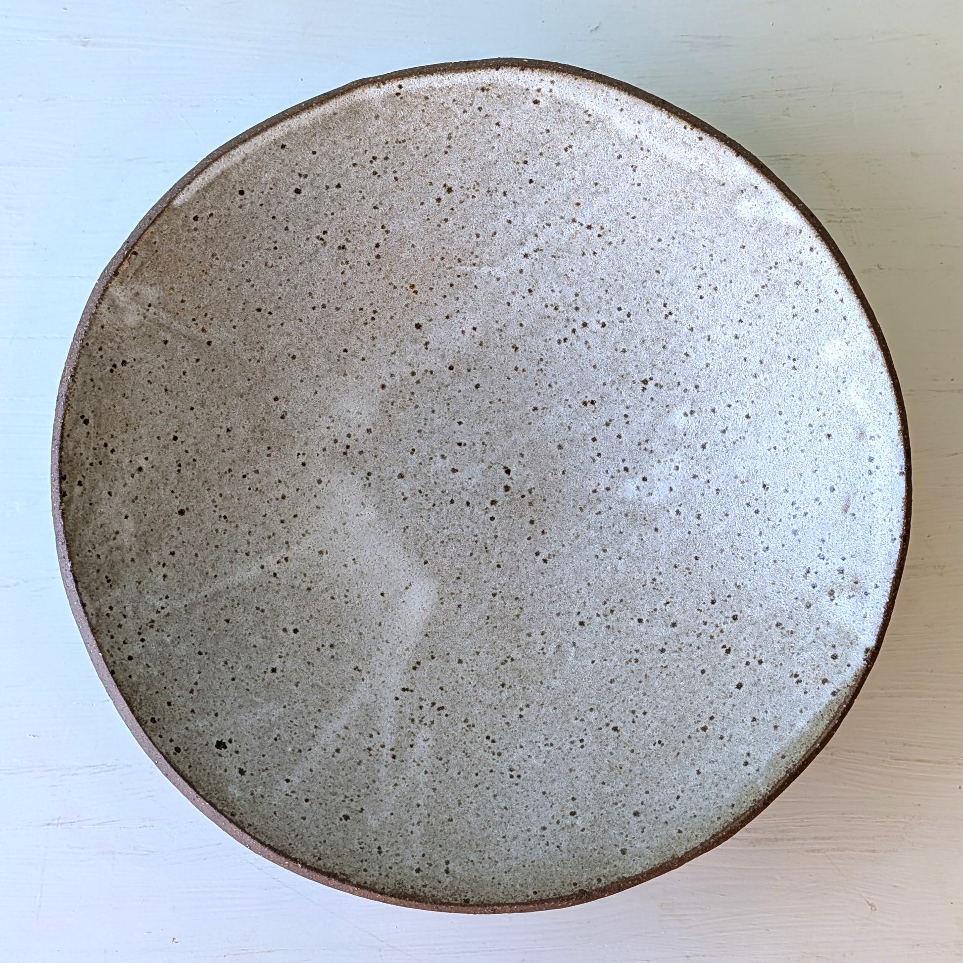 Round ceramic bowl with a speckled texture on a light blue background