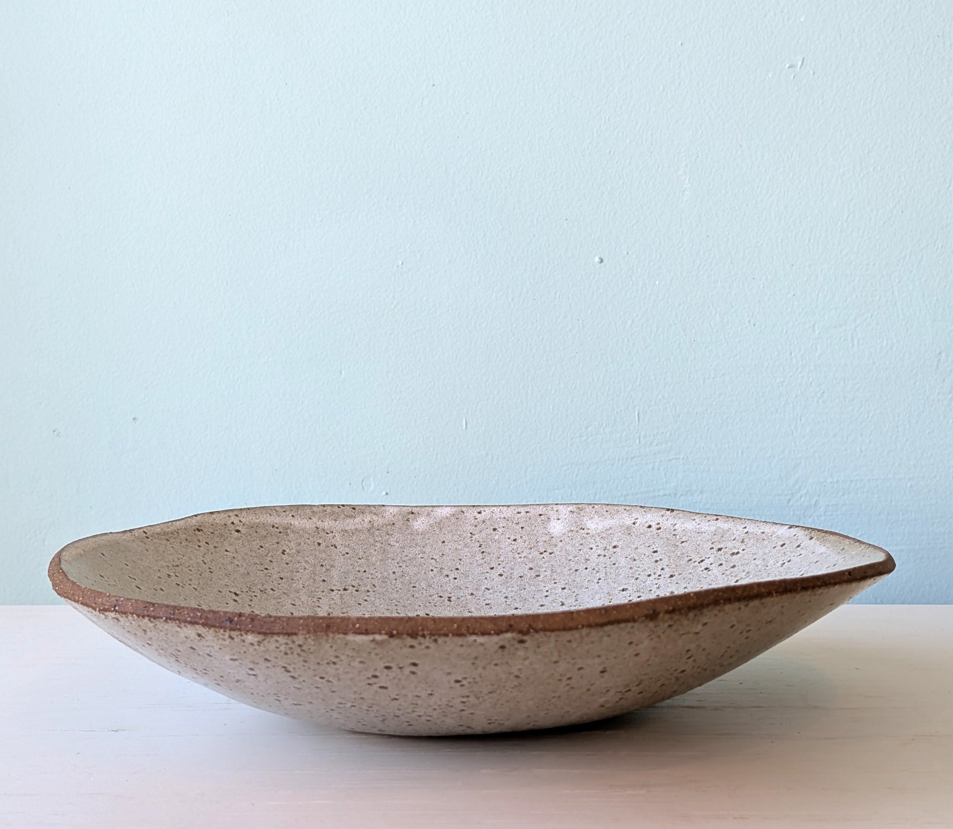 Large speckled ceramic bowl on white surface against a blue background.