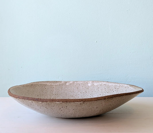 Large speckled ceramic bowl on white surface against a blue background.