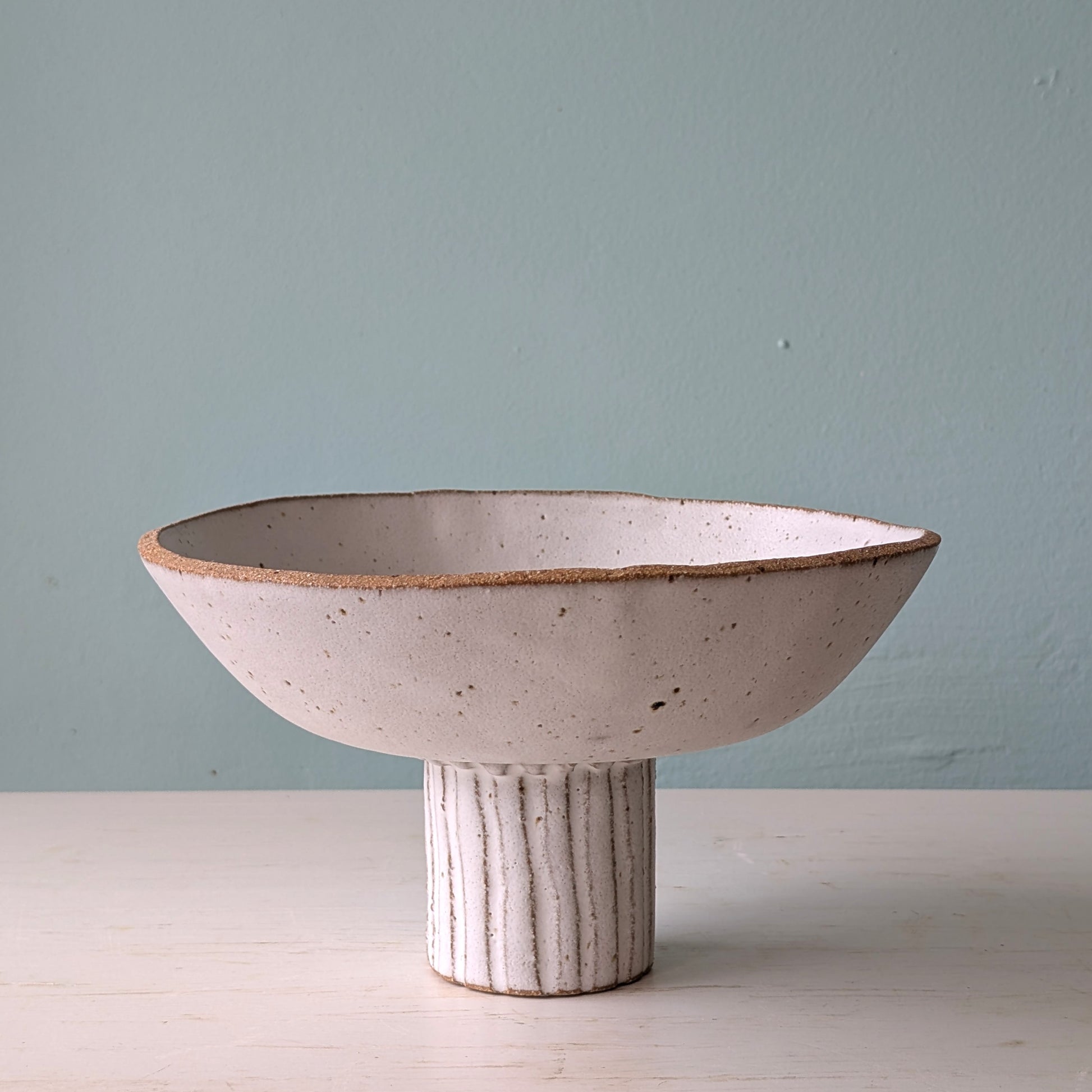 Ceramic bowl with a pedestal base on a light surface against a light blue wall