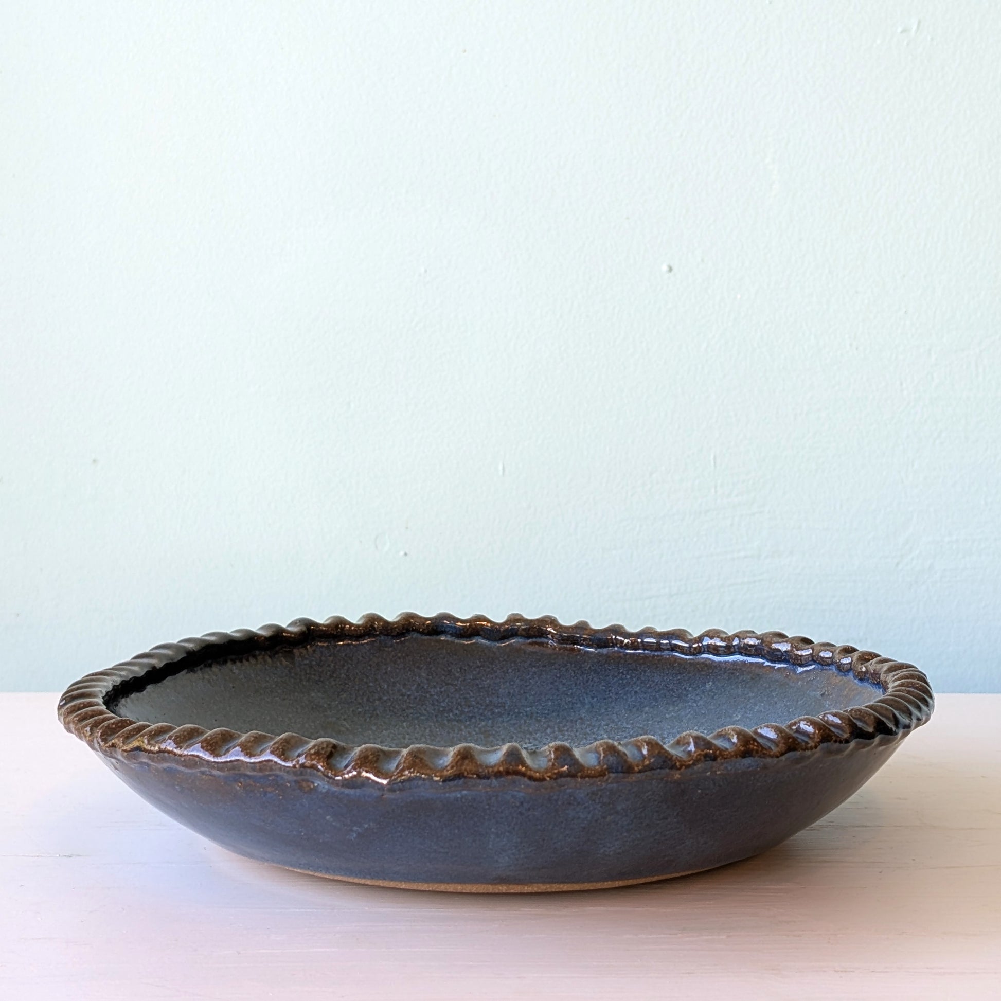 Blue ceramic bowl with textured rim on a light surface and light blue background