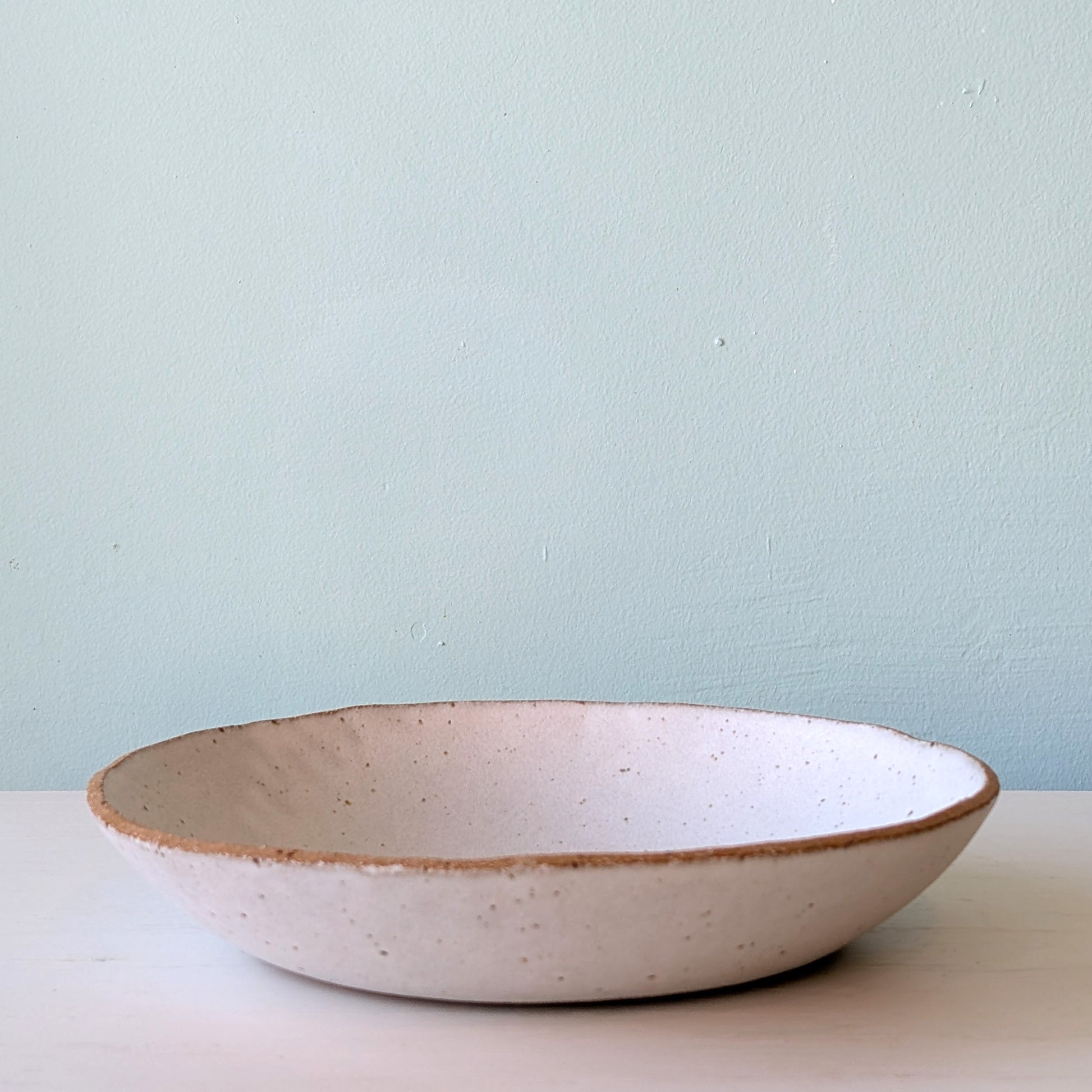 Ceramic bowl with speckled texture on a light surface against a light blue wall