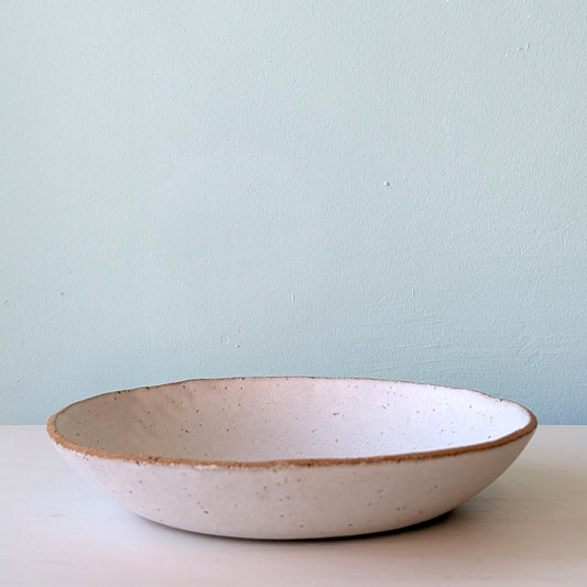Ceramic bowl with speckled texture on a light surface against a light blue wall