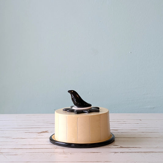 Round ceramic butter dish with black decorative elements on a light wooden surface and light blue background