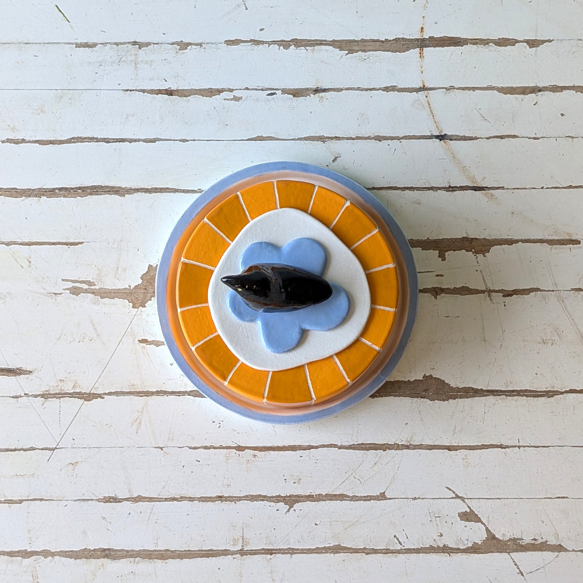 Top view of a colourful ceramic butter dish with a bird handle on a wooden surface.