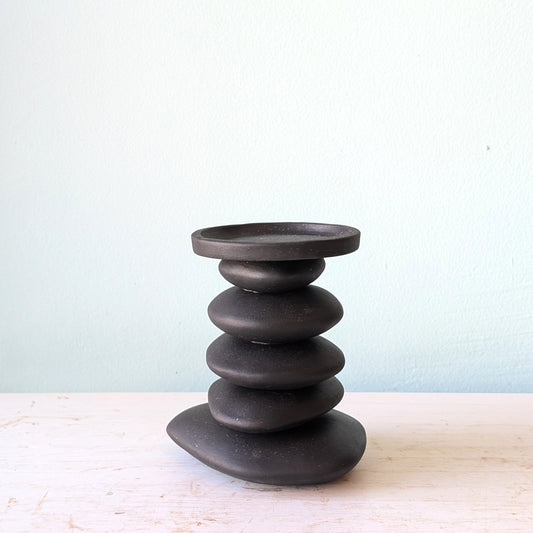 A black ceramic stack candlestick displayed on a light-colored wooden surface against a pale blue wall.