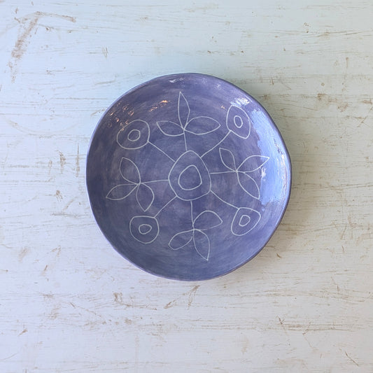 Purple ceramic plate with carved floral patterns on a light wooden surface