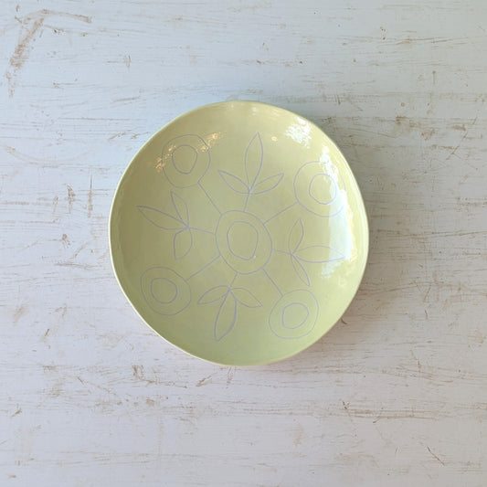 Yellow ceramic plate with carved floral design on a light wooden surface