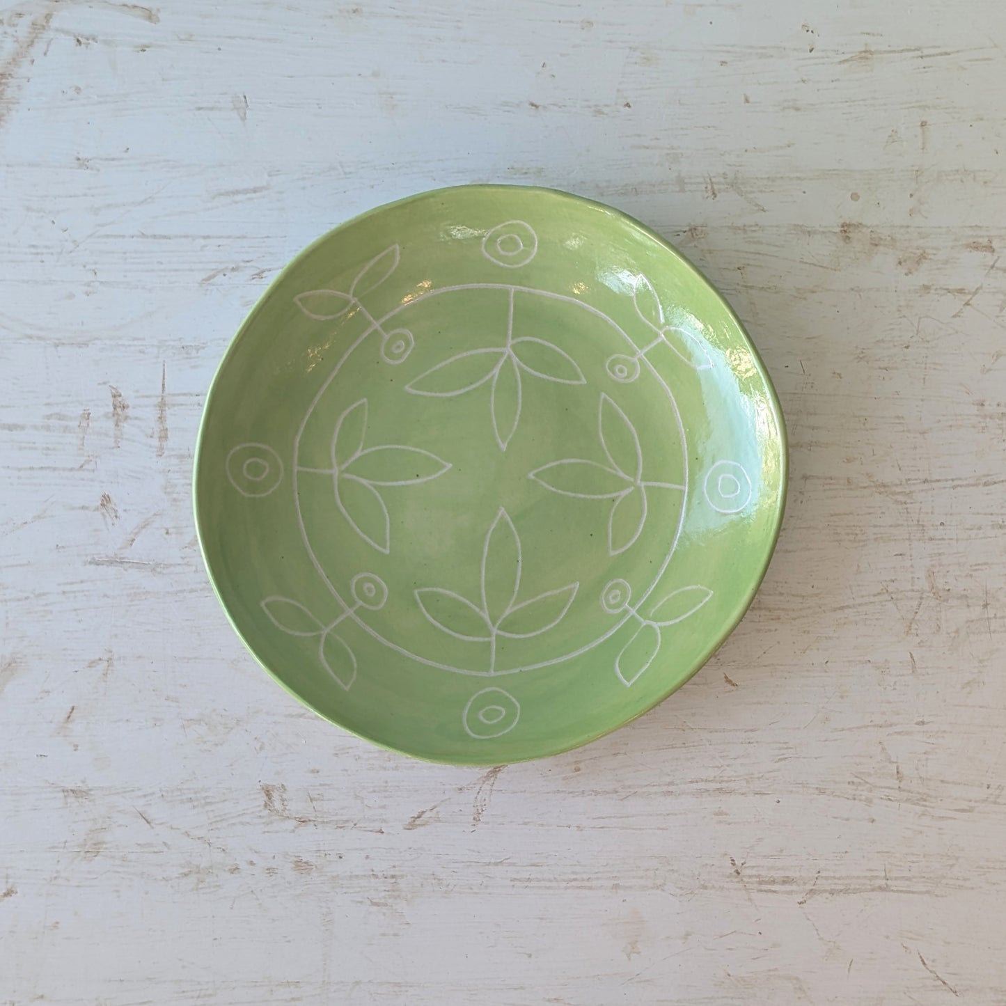 Green ceramic plate with carved floral design on a white wooden table.