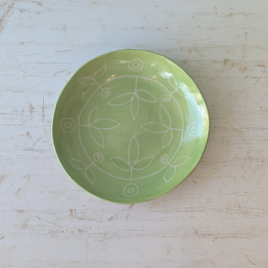 Green ceramic plate with carved floral design on a white wooden table.