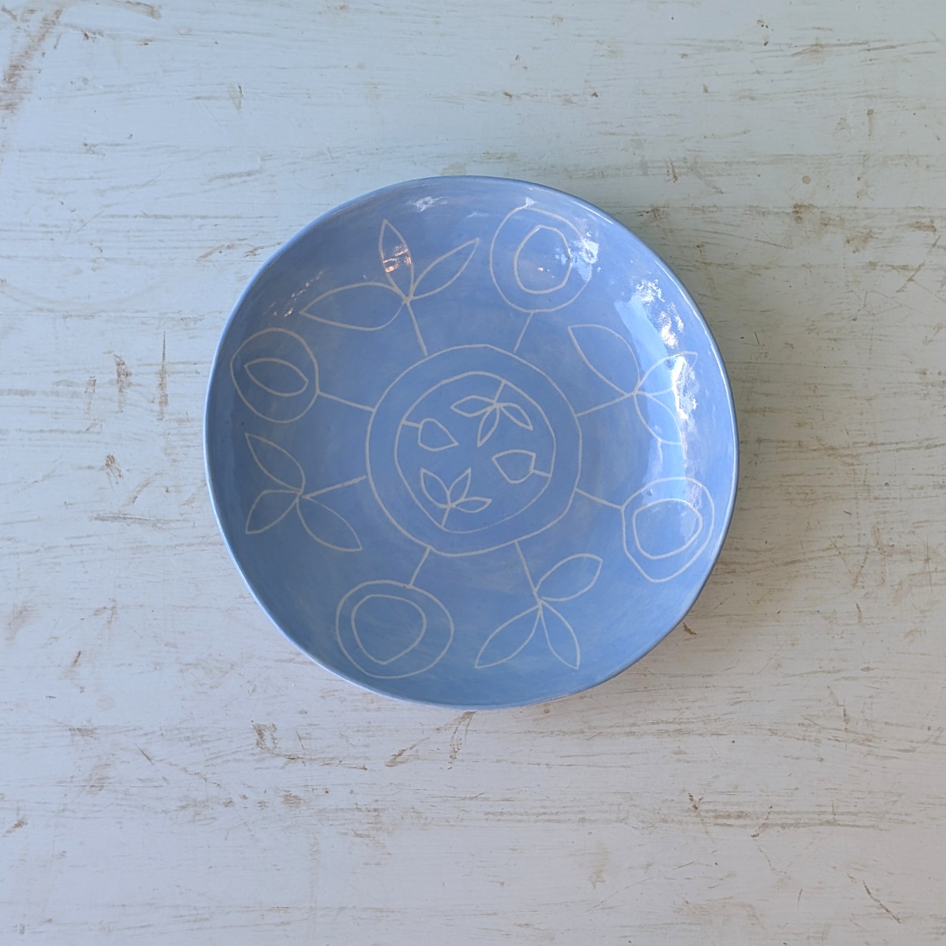 Blue ceramic plate with carved floral design on a white wooden table.
