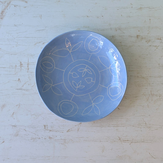 Blue ceramic plate with carved floral design on a white wooden table.