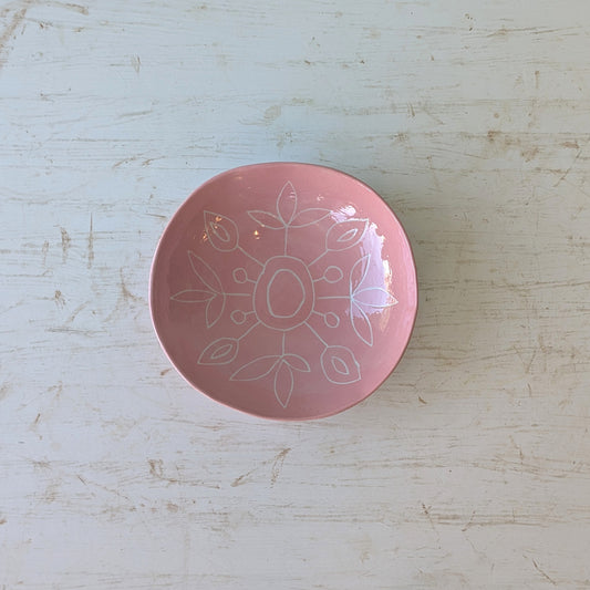 Pink ceramic plate with carved floral design on a light wooden surface