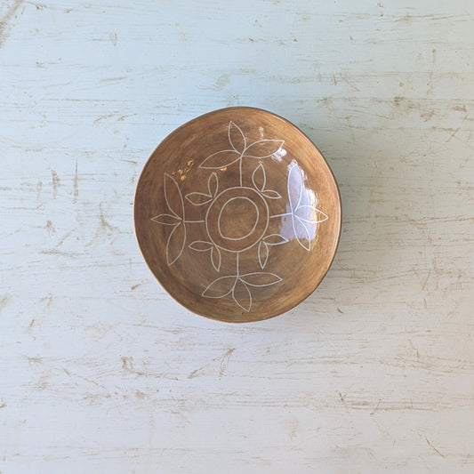 Small brown ceramic plate with floral carvings on a white wooden table